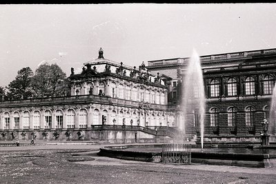 Neoclassical palace with grand arched colonnades and a prominent central dome, flanked by symmetrical wings. A large fountain...
