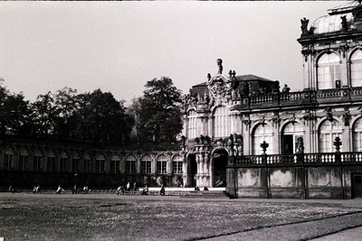 Baroque-style palace courtyard with ornate wrought-iron fence and classical statues. Symmetrical architecture features arched...