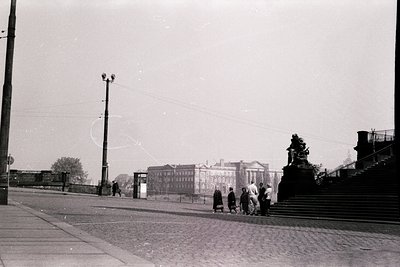 Black-and-white street scene featuring a group of children playing near a grand neoclassical building with columns, likely a ...