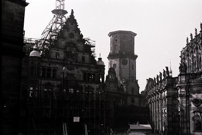 Black-and-white shot of a bombed European cathedral façade, 1940s. Intricate Gothic spires and clock tower partially intact a...