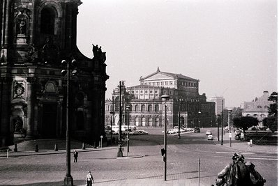 Historic urban scene featuring Baroque-style church façade with ornate sculptures and arched windows. Prominent classical the...