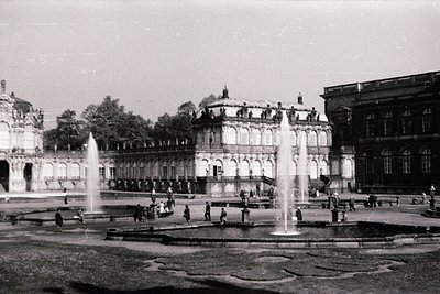 Neoclassical palace courtyard with symmetrical fountain design, likely 19th-century European architecture. Grand columns, arc...