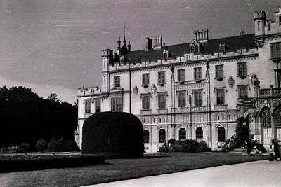 Neoclassical mansion with symmetrical façade, tall windows, and decorative stonework, set in a manicured garden. Likely Europ...