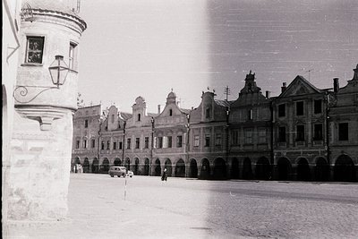 Historic European town square with Renaissance-style arcaded buildings, likely 1950s–1960s. Ornate gables, arched ground floo...