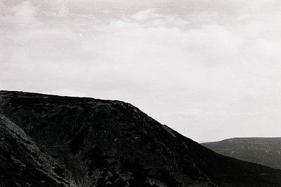 Monochrome landscape featuring jagged volcanic terrain with sharp ridges and dark, textured rock formations. Overcast sky cre...