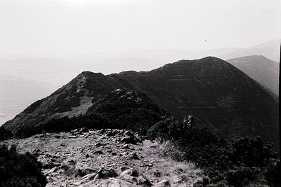 Black-and-white aerial view of rugged coastal terrain with steep slopes and sparse vegetation, likely a volcanic formation. D...