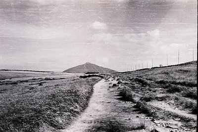 Mid-20th century black-and-white coastal landscape featuring a winding dirt path leading toward a solitary hill in the distan...