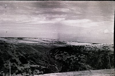 Vintage black-and-white landscape showing rugged, terraced hills with sparse vegetation under a cloudy sky. Horizontal framin...