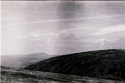 Vintage black-and-white landscape featuring rolling hills with sparse vegetation under a cloudy sky. Horizontal scan lines su...
