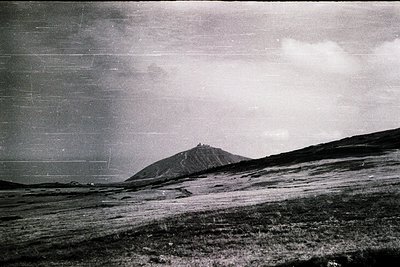 Vintage black-and-white landscape featuring a lone, conical hill rising from a flat, grassy plain under stormy skies. Minimal...
