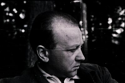 Portrait of a balding man in mid-profile, captured in high-contrast black-and-white. His expression appears contemplative, se...