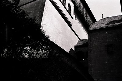 Striking black-and-white shot of Brutalist architecture—exposed concrete walls and angular roofline framed by dense foliage. ...