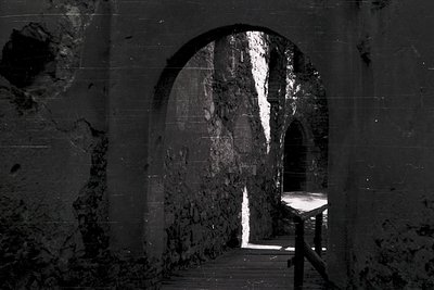 Monolithic stone tunnel with arched openings, illuminated by natural light filtering through cracks. Rough-hewn walls and flo...