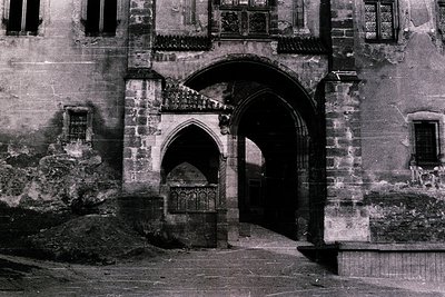 Historic stone archway with Gothic revival details—pointed arches, decorative keystones, and weathered brickwork. Likely Euro...