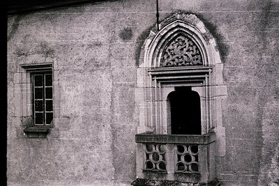 Gothic-style stone facade featuring a pointed arch doorway with intricate tracery above and a small rectangular window to the...