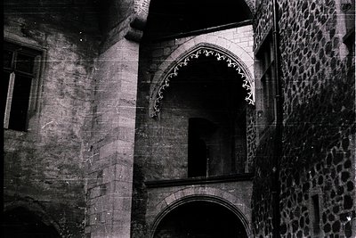 Gothic-style arched doorway framed by weathered stone walls, featuring intricate tracery above. Likely European medieval arch...