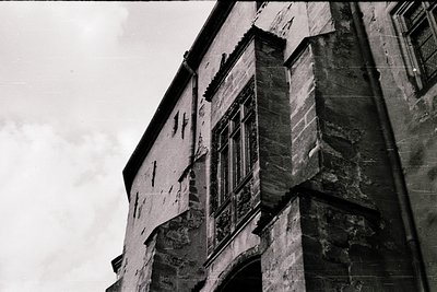 Monochrome shot of a weathered stone building corner with exposed brickwork and arched window frames. Architectural details s...