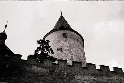 Historic stone watchtower with conical roof atop fortified wall, likely medieval European. Distinctive crenellated battlement...