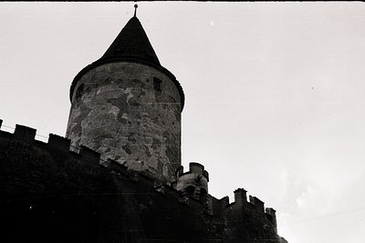 Mid-century black-and-white shot of a medieval stone tower with conical roof, likely part of a castle or fortress. Weathered ...