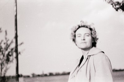 Black-and-white portrait of a woman in mid-20th-century fashion, wearing a high-necked coat and short, voluminous hairstyle. ...