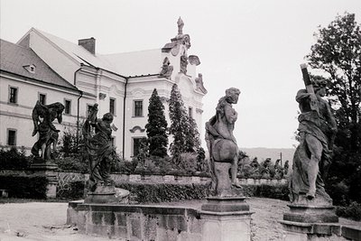 Baroque-style fountain with four dynamic stone figures—two kneeling, one seated on horseback, and one standing—surrounding a ...