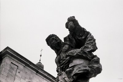 Monumental stone sculpture depicting a seated figure cradling another, likely maternal/child theme. Architectural backdrop su...