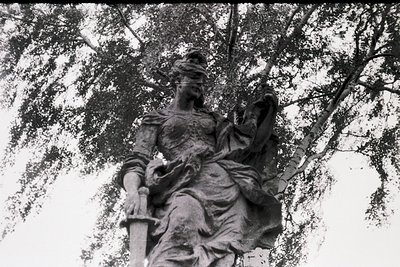 Neoclassical stone statue of a draped female figure holding a sword, likely a war or victory allegory. Intricate drapery and ...