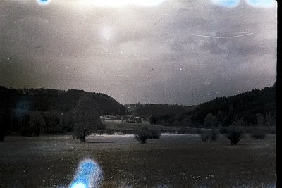 Vintage sepia-toned landscape shot through a window, showcasing a rural valley with dense forest on either side. Overcast sky...