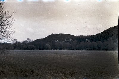Vintage sepia-toned landscape featuring open agricultural field with sparse vegetation, bordered by forested hills. Early 20t...