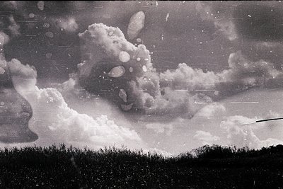 Vintage black-and-white shot of a dramatic mushroom cloud rising over flat terrain, likely from a nuclear test. Distinctive s...