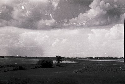 Dramatic low-angle shot of storm clouds over flat, open landscape with lone tree and distant horizon. Black-and-white composi...