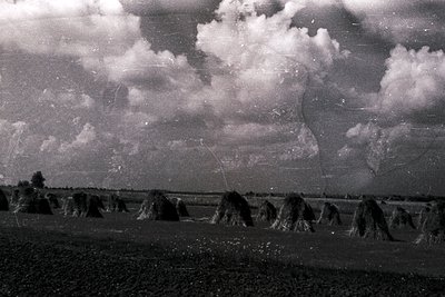 Vintage black-and-white rural landscape featuring stacked hay bales in neat rows under dramatic, textured clouds. Evidence of...