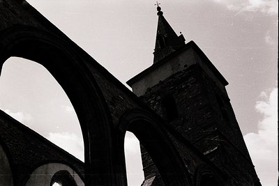 Gothic stone archway framing a church steeple with intricate masonry details. Dramatic low-angle composition highlights archi...