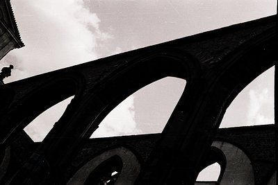 Black-and-white shot of a grand stone bridge arch framing sky and clouds. Architectural details highlight intricate masonry a...