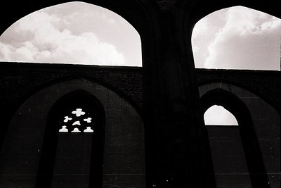 Symmetrical stone arches frame a dramatic sky with clouds mirrored in a reflective surface below. The central panel displays ...
