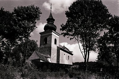 Mid-20th century rural church with onion dome and bell tower framed by dense foliage. Brick construction with arched windows ...