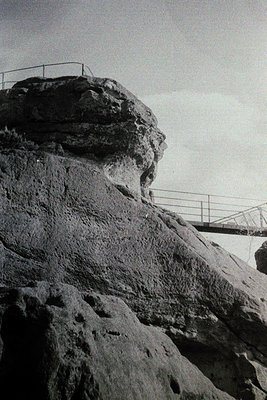 Monolithic rock formation with a metal walkway atop, framed by rugged cliffs. Mid-century engineering meets natural landscape...