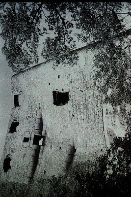Vintage black-and-white photo of a weathered stone building with visible cracks and missing sections, likely a historic ruin....