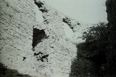 Monochrome close-up of weathered stone ruins, likely ancient or medieval masonry. Irregular, roughly cut blocks with visible ...