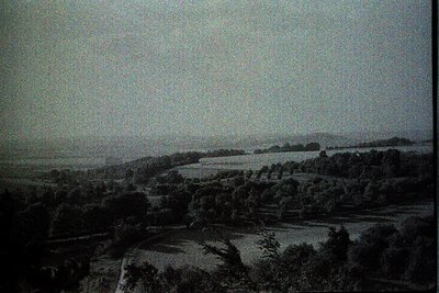 Vintage sepia-toned landscape featuring rolling hills, dense tree clusters, and winding rural roads. Low-contrast monochrome ...