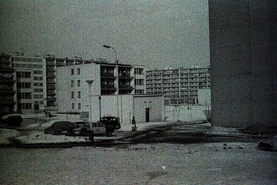 Mid-century urban scene featuring Soviet-era Brutalist apartment blocks with flat roofs and concrete balconies. Snow covers g...