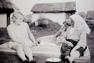 Vintage black-and-white photo of three women seated on a wooden bench in rural outdoor setting. Left: woman in 1940s-style dr...