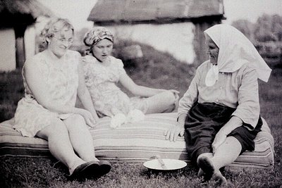 Three women seated outdoors on a striped blanket, mid-20th century. Left: young woman in sleeveless dress, center: child in h...