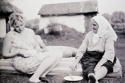 Black-and-white photo of two women seated outdoors on a striped blanket, likely mid-20th century. The younger woman wears a s...