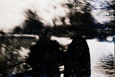 Vintage monochrome photo of two figures in motion, blurred by motion or low focus. Likely candid street or urban scene from m...