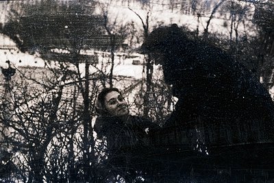 Vintage sepia-toned portrait of a seated man in a forest, framed by bare winter branches. His posture suggests contemplation ...