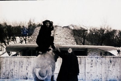 Black-and-white snapshot of two children atop a snow-covered concrete wall, likely mid-20th century. Child on left balances o...