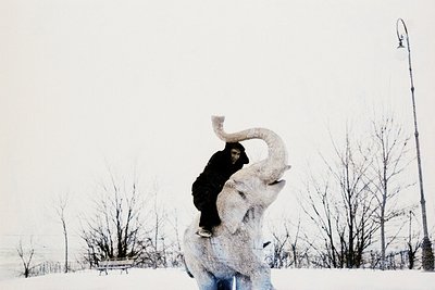 Black-and-white photo of a person mid-air performing a daring stunt atop a large, white elephant statue. The scene captures m...
