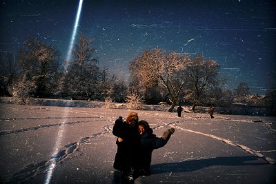 Two figures ice skate on a frozen lake under a bright comet streak, surrounded by leafless trees. Warm light casts long shado...