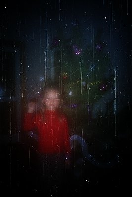 Silhouetted figure in a red coat standing under illuminated rain at night, with blurred light trails from falling water dropl...
